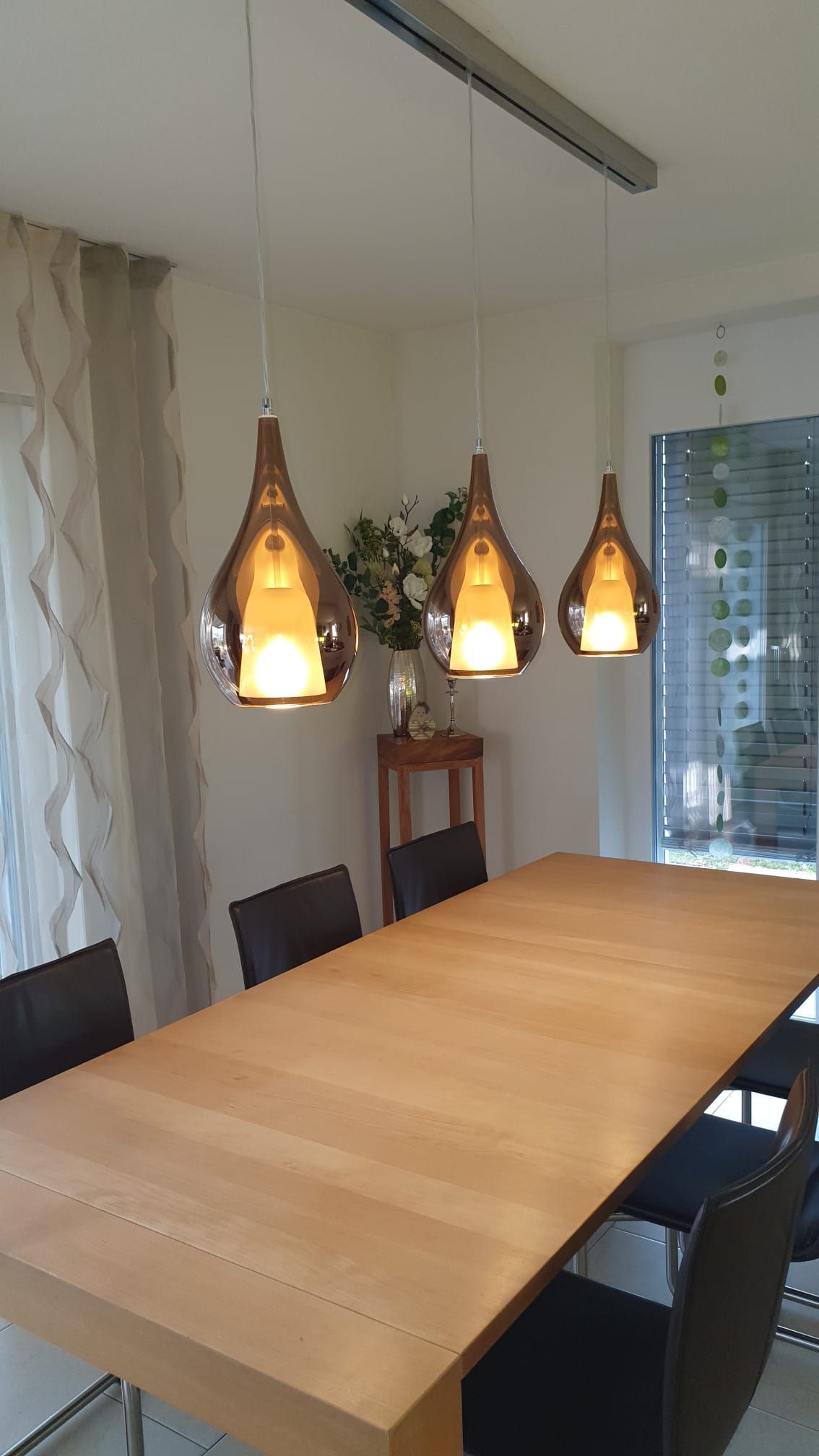 Ein Esszimmer mit einem Holztisch und Stühlen und drei Pendelleuchten, die von der Decke hängen.