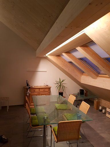 Ein Esszimmer mit einem Glastisch und Stühlen auf einem Dachboden.