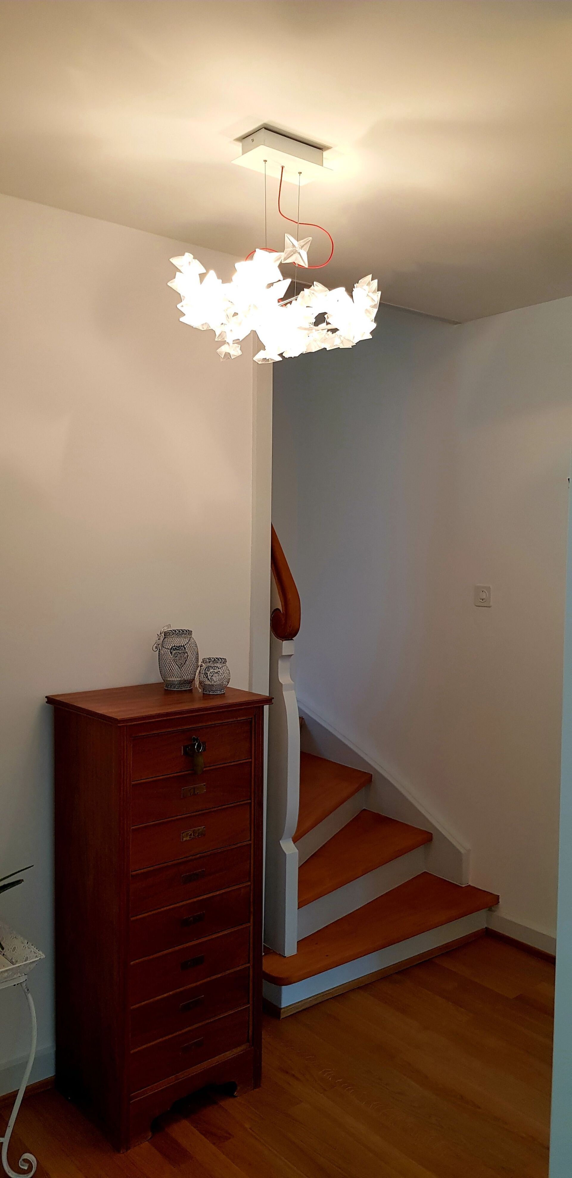 Ein Flur mit Treppe, einer Kommode und einem Kronleuchter, der von der Decke hängt.