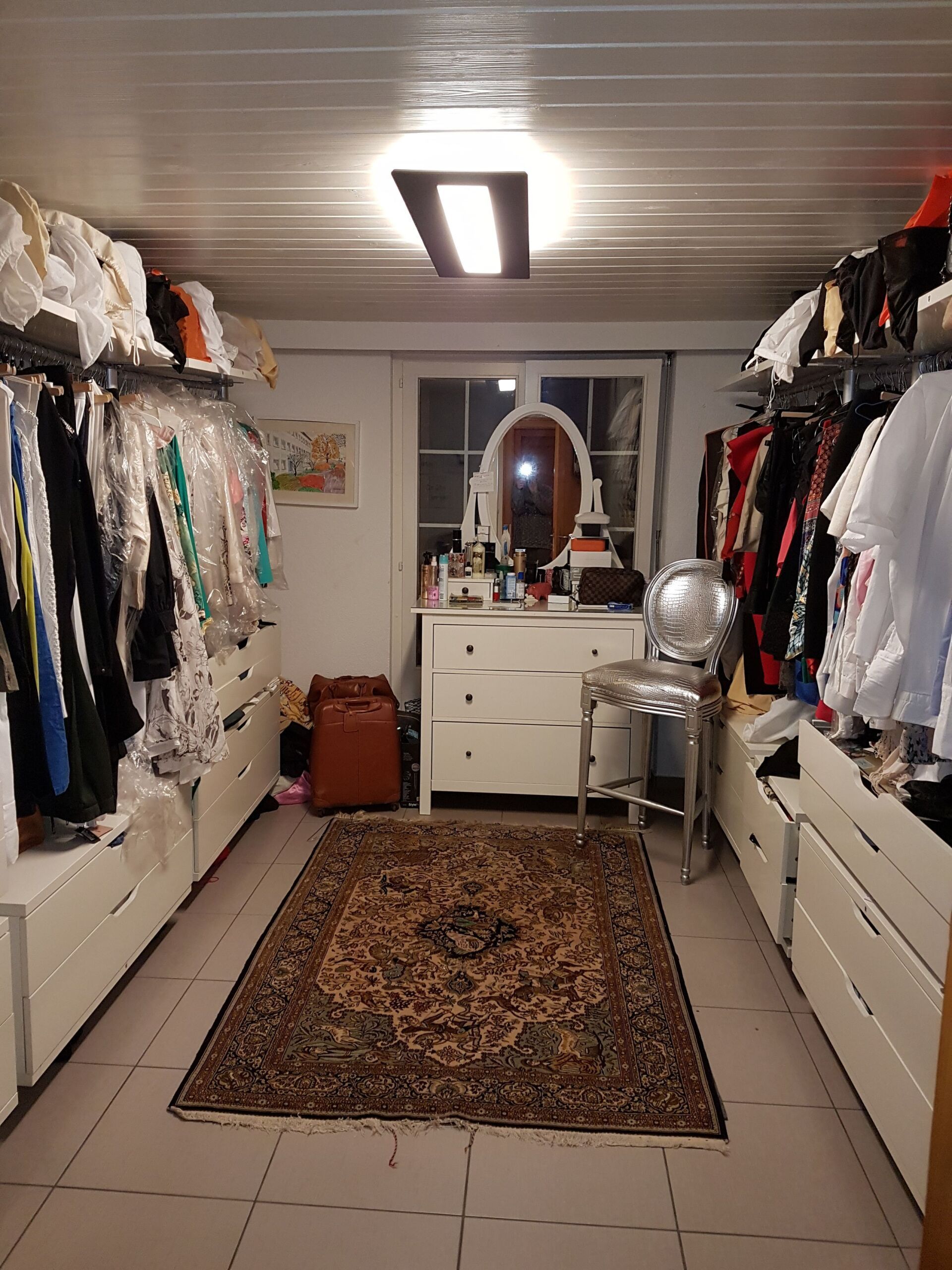 Ein großer begehbarer Kleiderschrank voller Kleidung und einem Teppich.