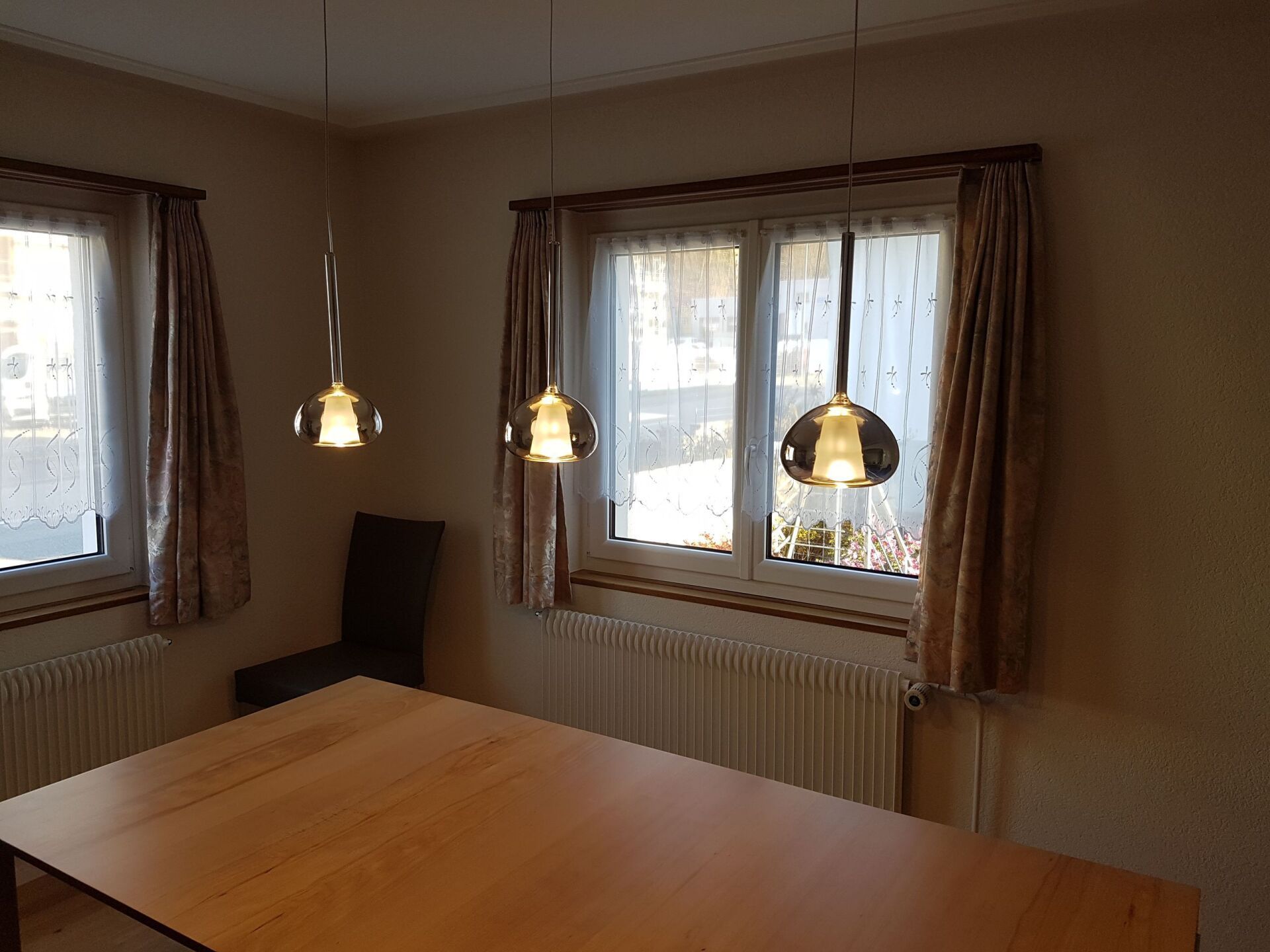 Ein Esszimmer mit einem Tisch, Stühlen und zwei Fenstern.