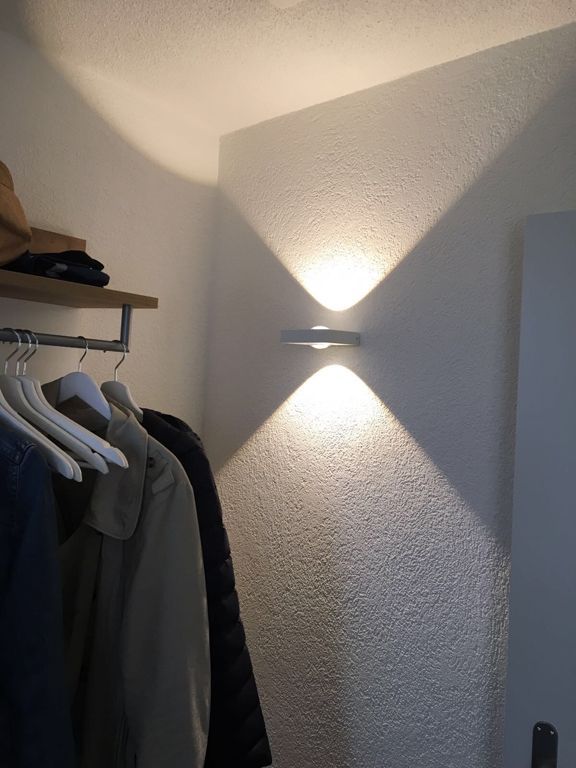 Ein Schrank mit an einer Stange hängender Kleidung und einer Lampe an der Wand.