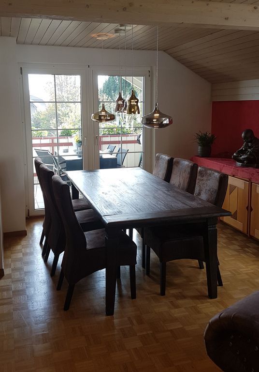 Ein Esszimmer mit einem langen Tisch und Stühlen vor einem Fenster.