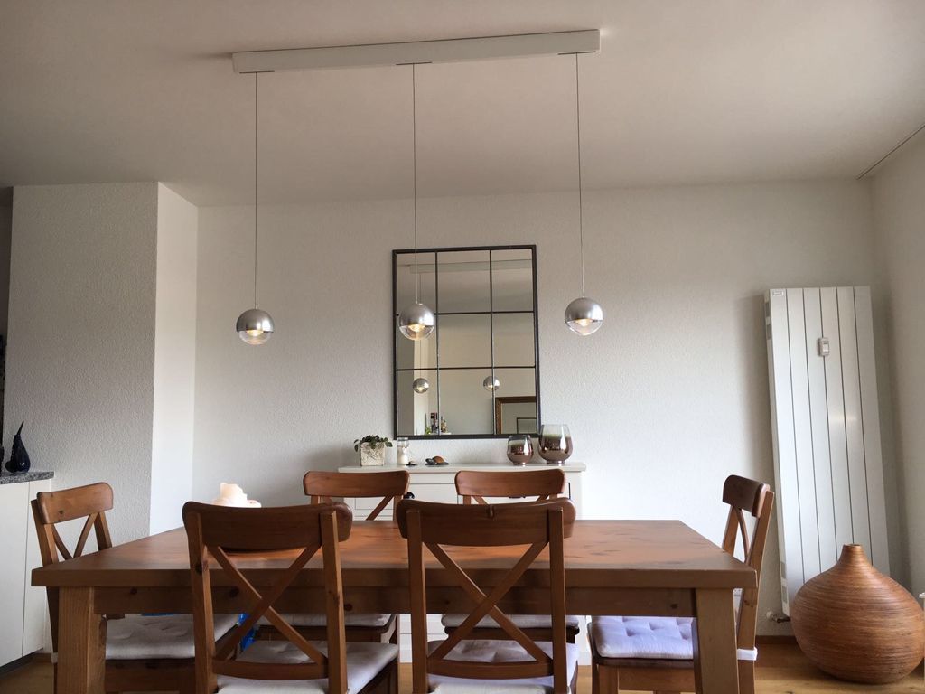 Ein Esszimmer mit einem Holztisch und Stühlen und einem von der Decke hängenden Spiegel.