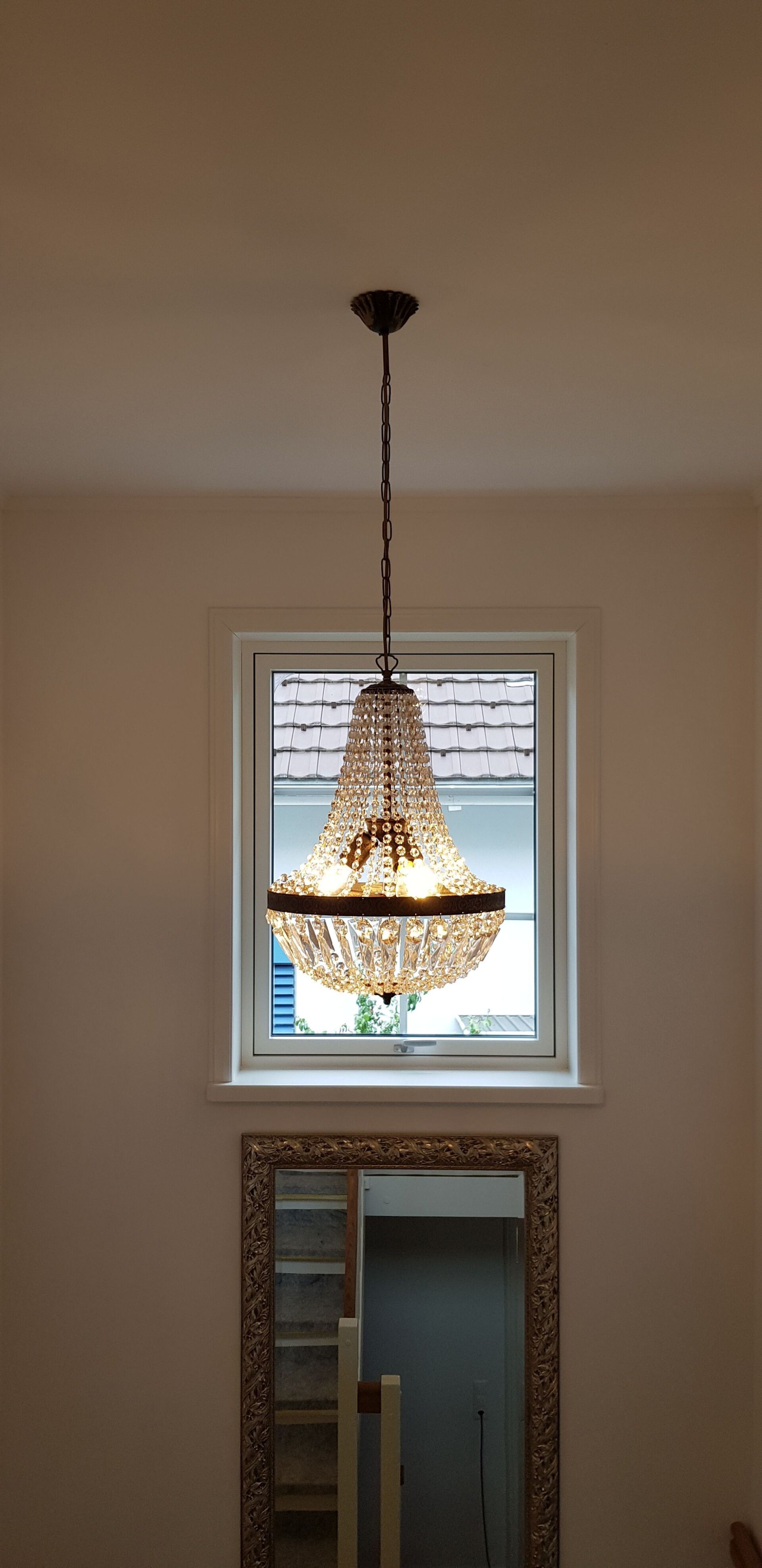 Vor einem Fenster hängt ein Kronleuchter von der Decke.