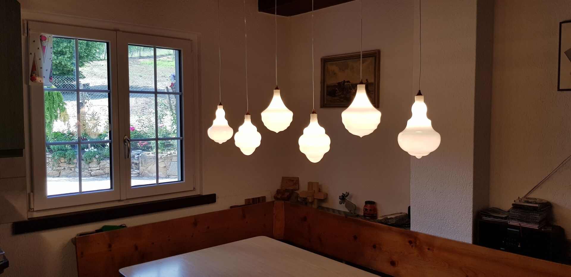 Ein Raum mit einem Tisch und einem Fenster, von dessen Decke ein paar Lichter hängen.