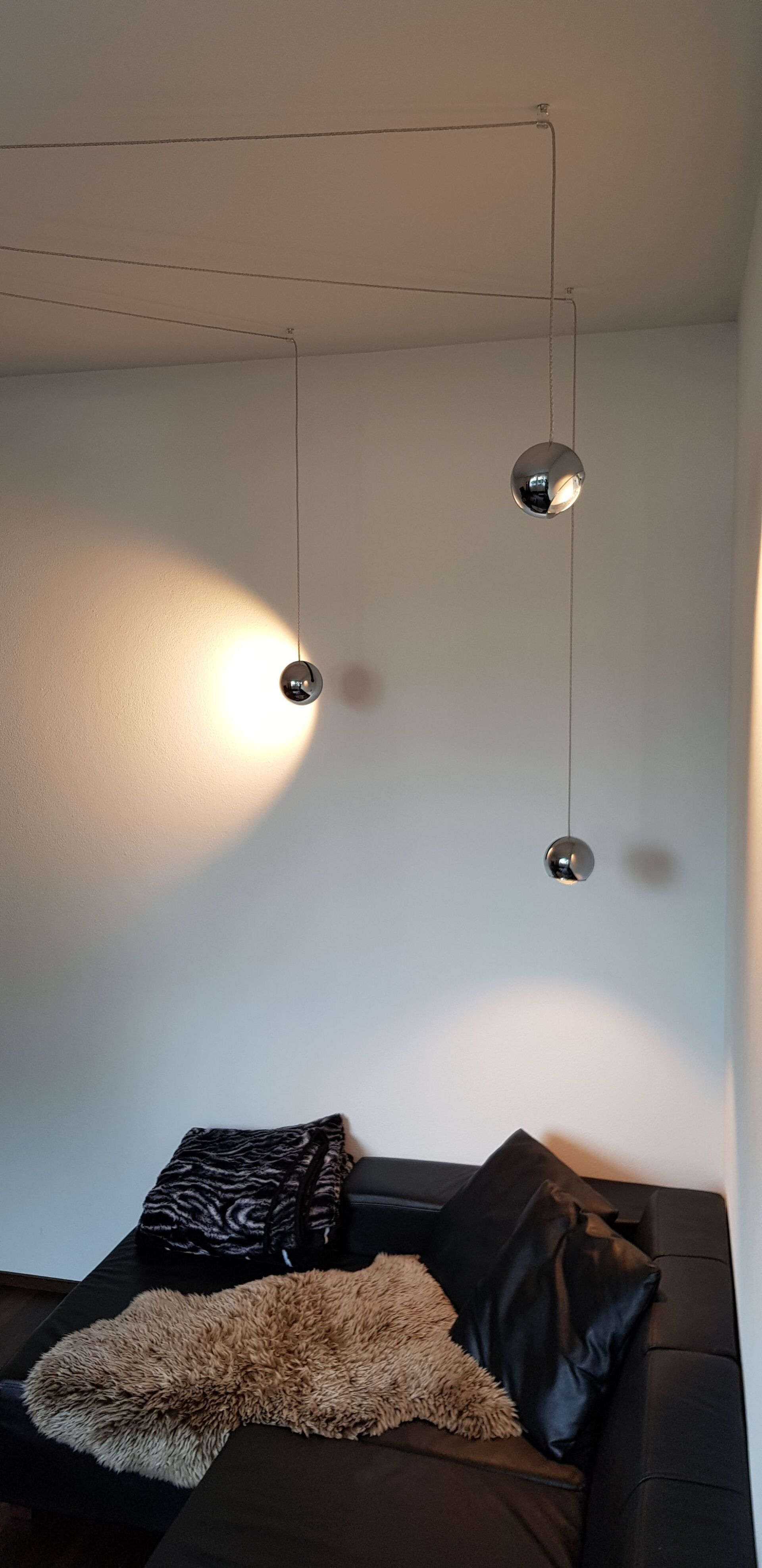 Ein Wohnzimmer mit einer schwarzen Couch und zwei Lampen, die von der Decke hängen.