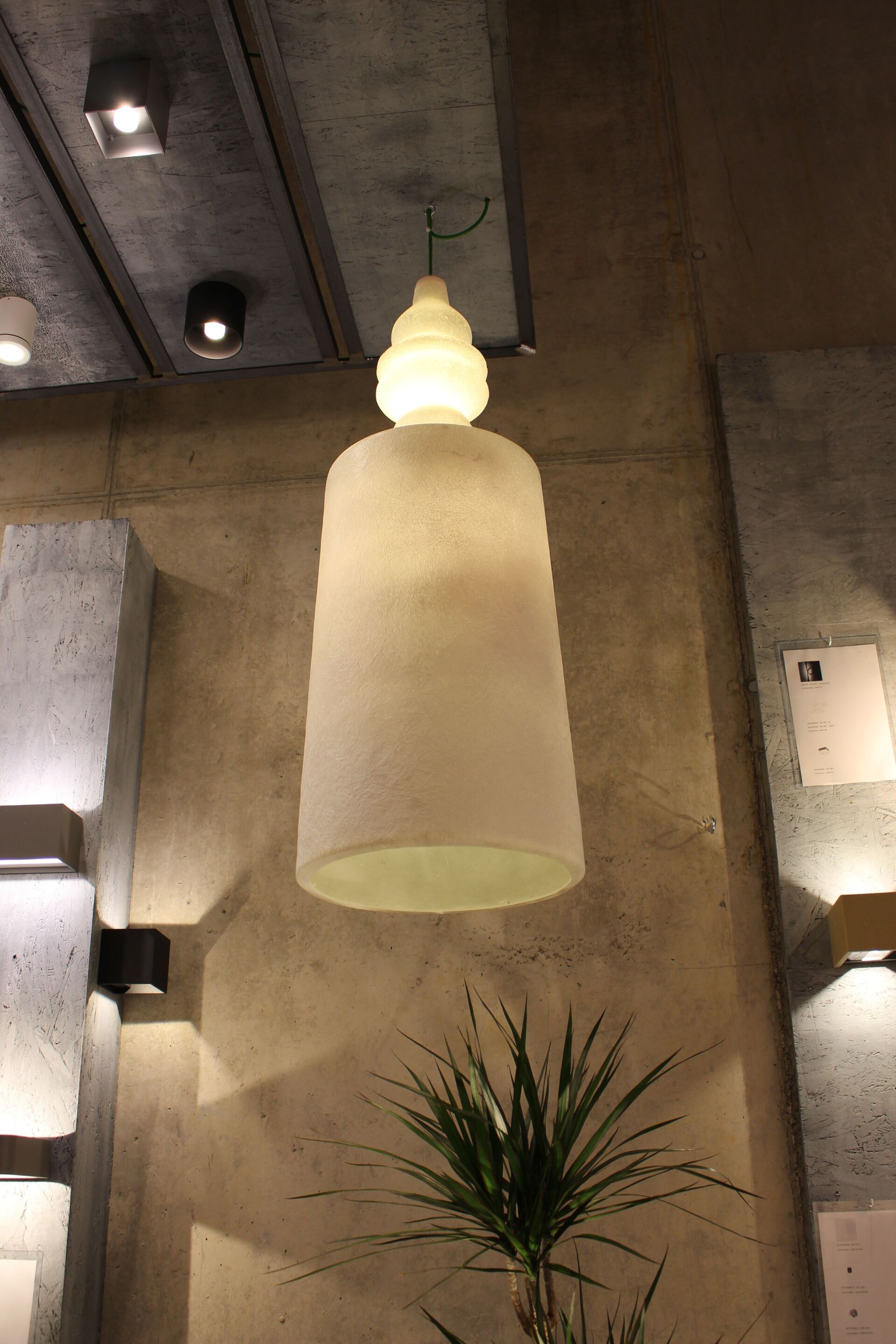 Eine weiße Pendelleuchte hängt neben einer Pflanze von der Decke.