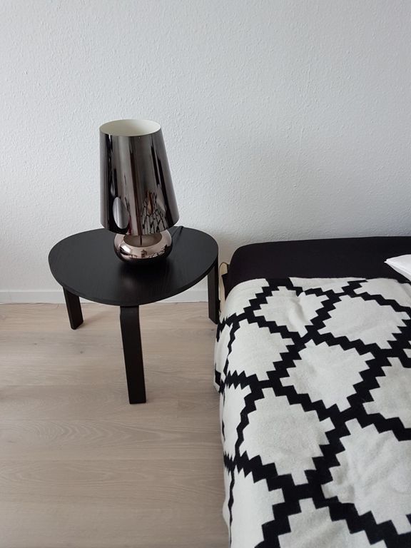 Ein Tisch mit einer Lampe darauf neben einem Bett