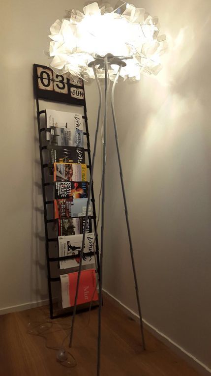 In einem Zimmer steht eine Lampe neben einem Zeitschriftenständer.