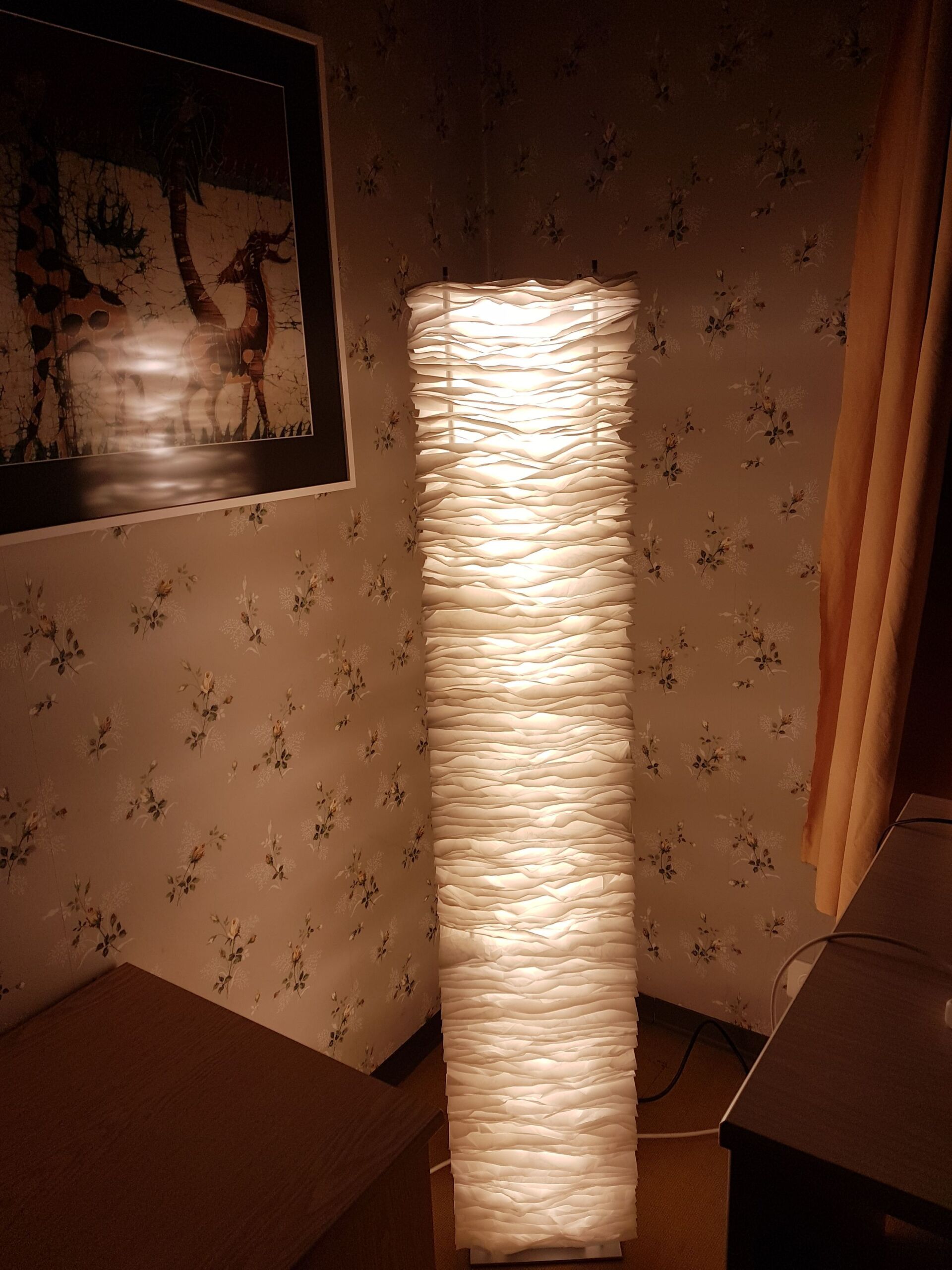 Eine große weiße Lampe steht in einem Raum neben einem Tisch.