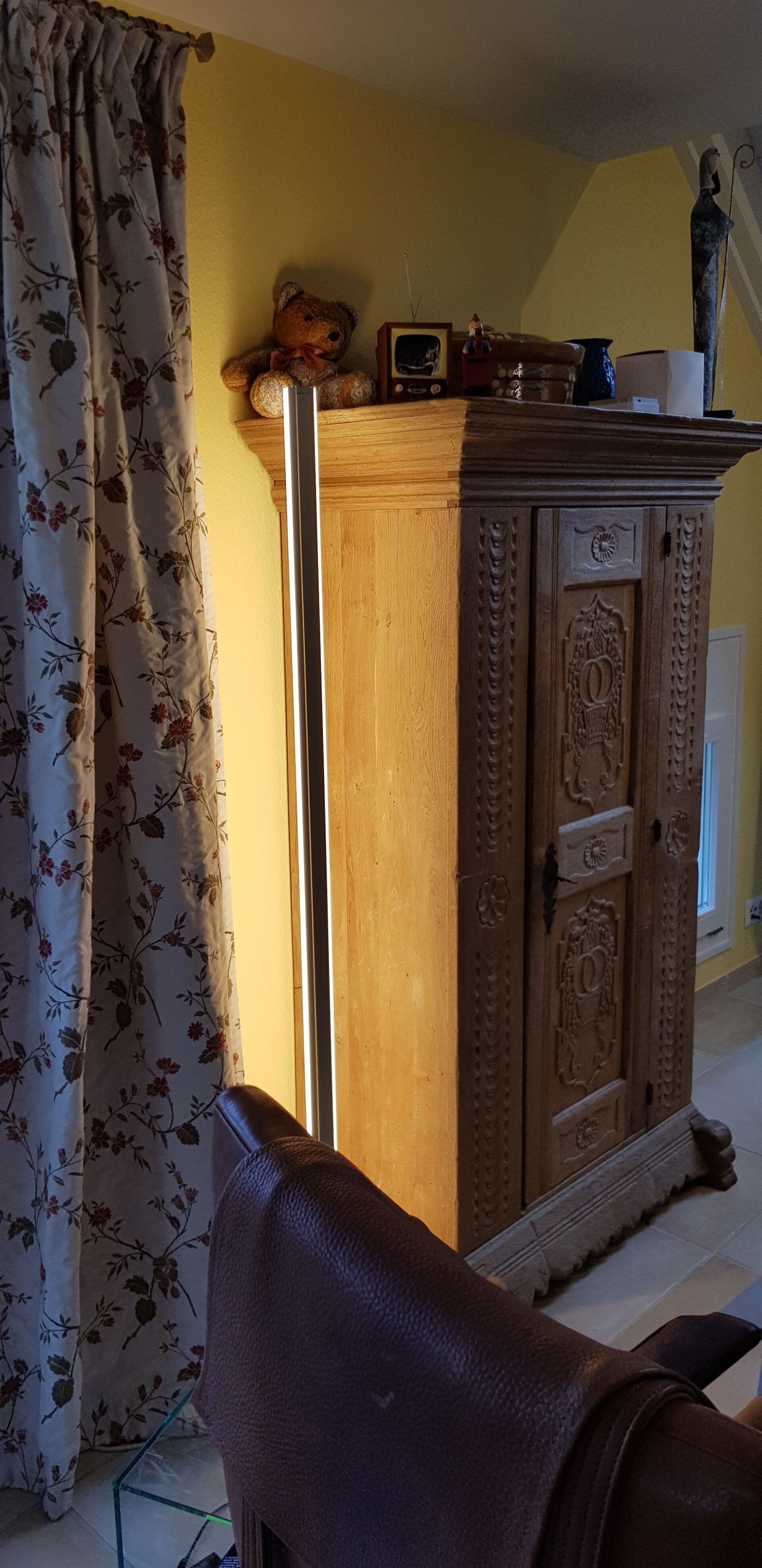 In einem Wohnzimmer steht ein Holzschrank neben einem Stuhl.