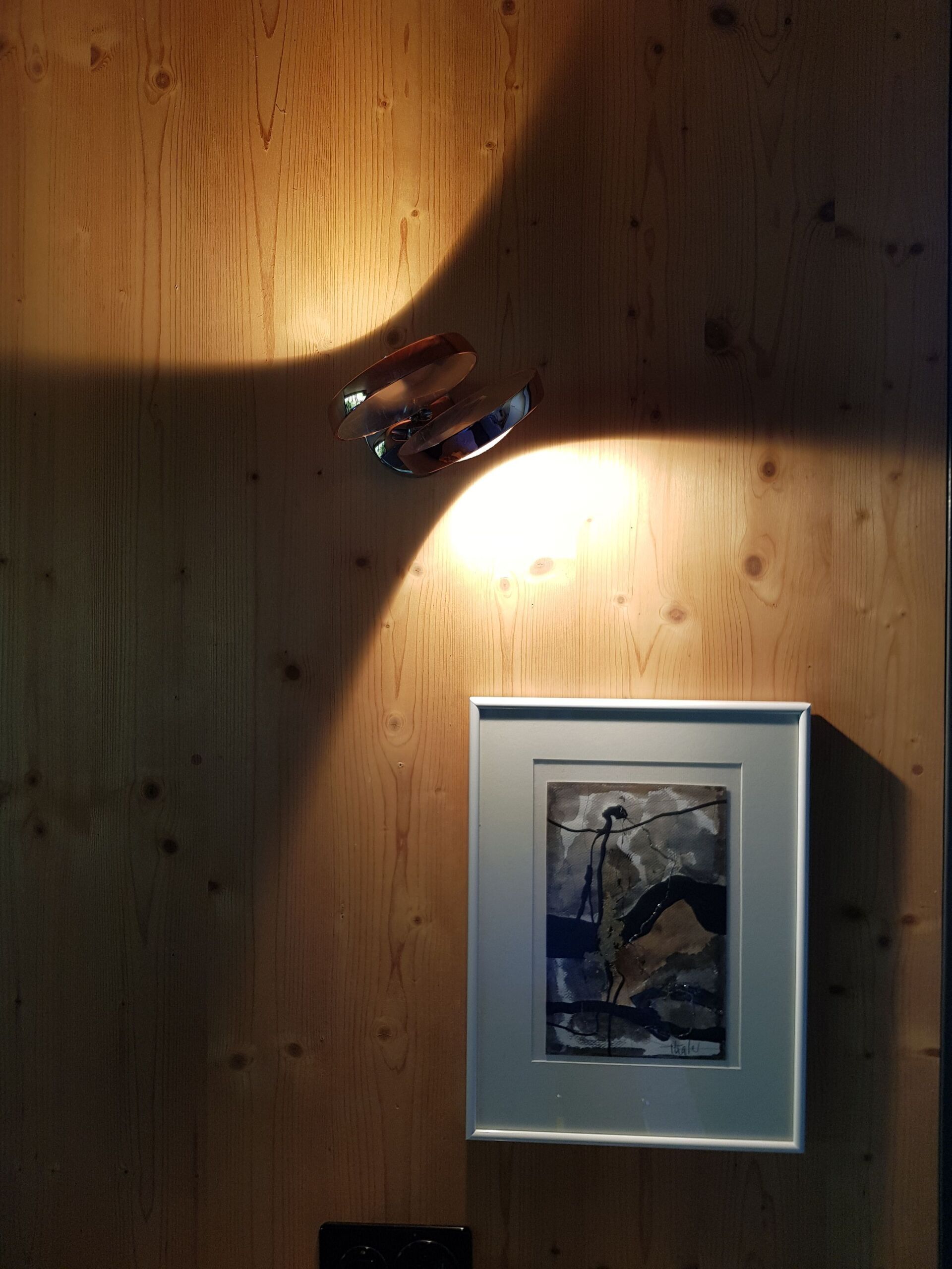 Ein Bild hängt an einer Holzwand neben einer Lampe