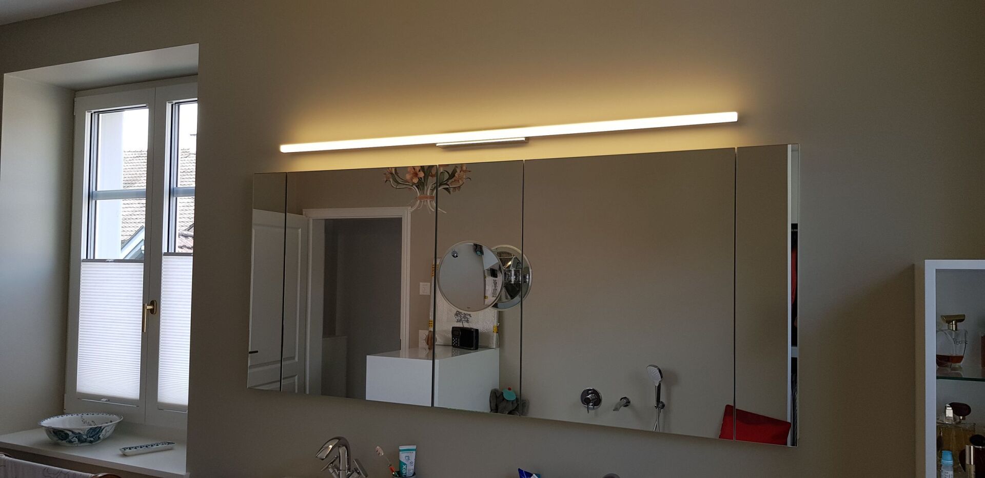 Ein Badezimmer mit großem Spiegel und Fenster.