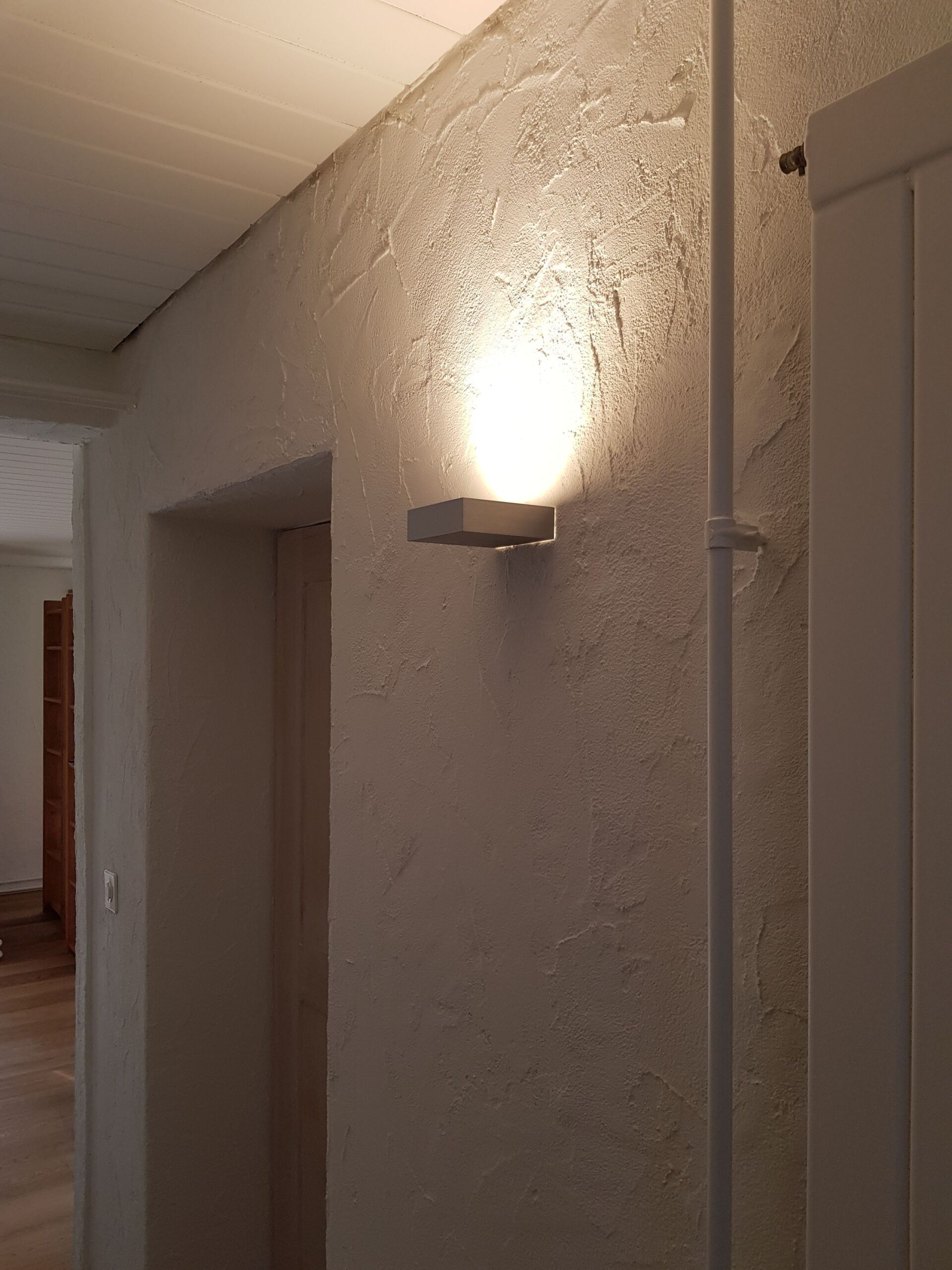 Ein Flur mit einer Wandlampe und einer Tür.