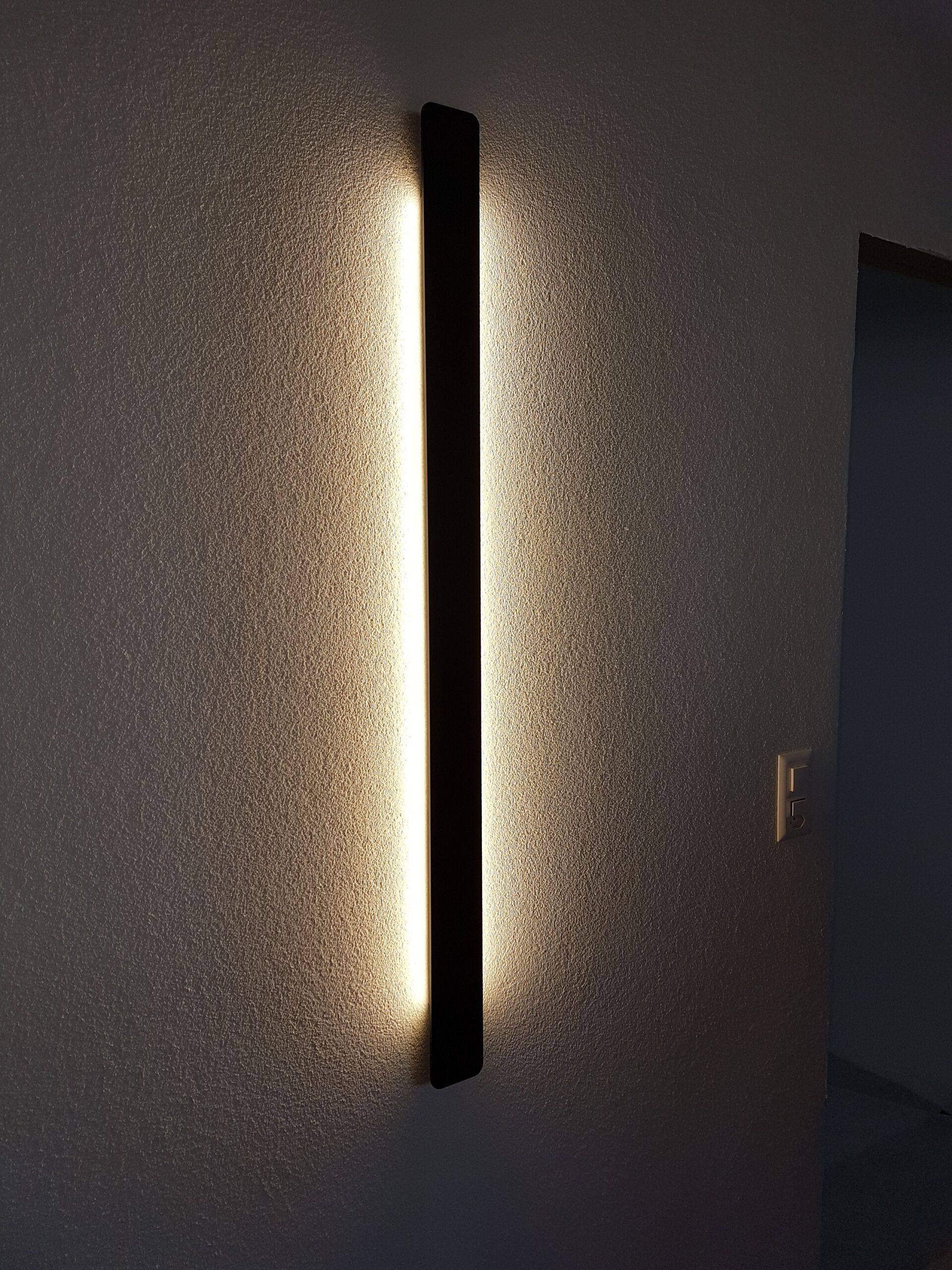 An einer Wand neben einer Tür hängt eine lange Lampe.