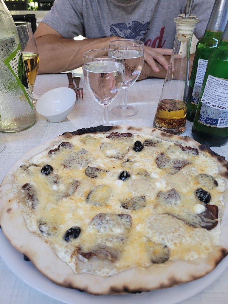 Une pizza base crème avec des champignons devant des verres et des bouteilles