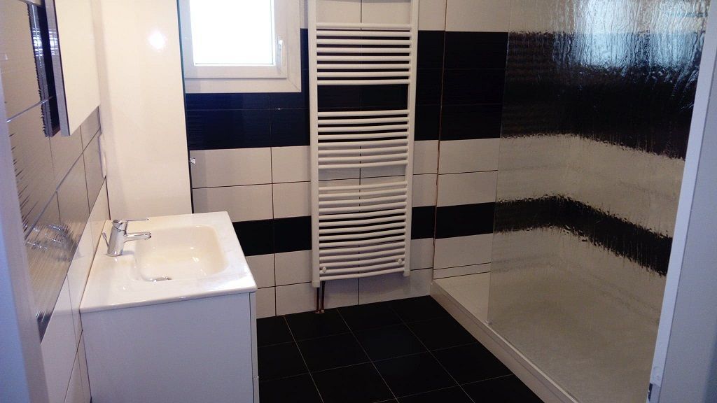 Une salle de bains moderne avec un meuble-lavabo blanc, un grand radiateur sèche-serviettes blanc et une douche vitrée sur un carrelage noir et blanc.