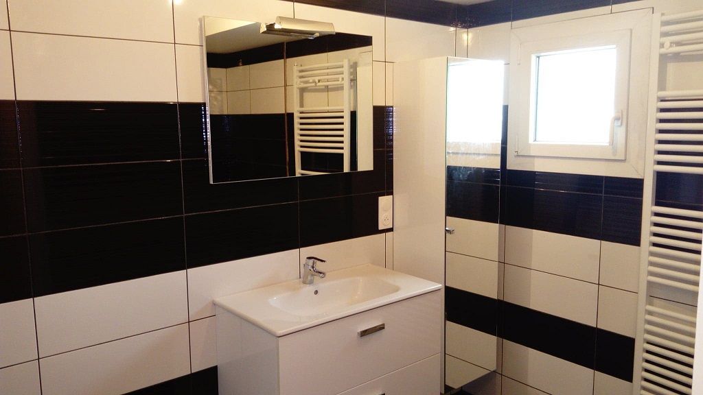 Une salle de bains moderne avec un meuble-lavabo blanc et un robinet argenté, un miroir rectangulaire et des murs carrelés en noir et blanc.