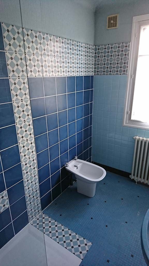 Salle de bains avec bidet adossé à un mur de carreaux carrés bleu foncé, un radiateur blanc et une frise de carreaux à motifs.