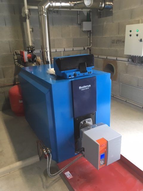 Une chaudière industrielle Buderus bleue avec un brûleur gris, installée dans un local technique aux murs en parpaings.