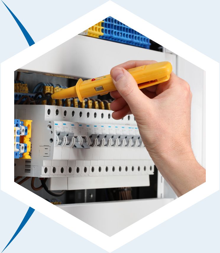 Une main utilise un testeur de tension jaune pour vérifier les connexions électriques d'un tableau de disjoncteurs.
