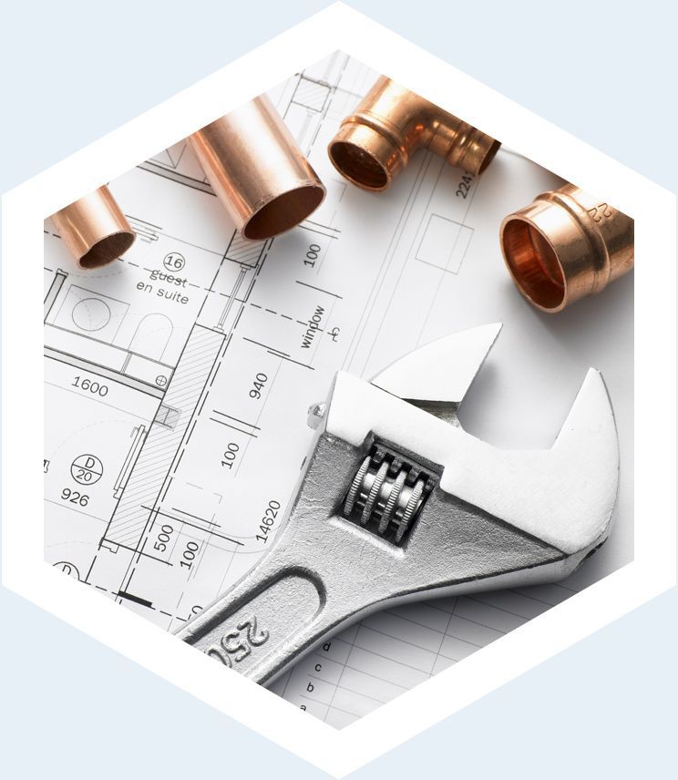 Des raccords de plomberie en cuivre et une clé à molette posées sur des plans architecturaux.