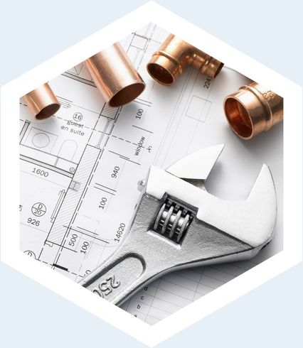 Des raccords de plomberie en cuivre et une clé à molette posées sur des plans architecturaux.