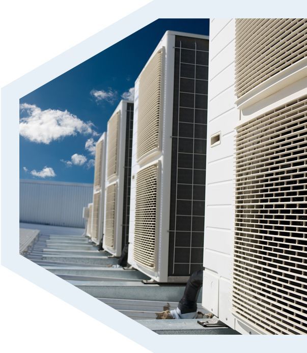 Une rangée d'unités de condensation extérieures blanches pour la climatisation se dresse sur un toit plat, se détachant sur un ciel bleu dégagé.