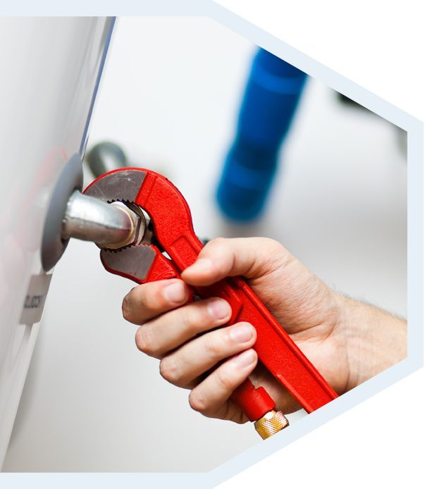 Une main utilise une clé à pipe rouge pour serrer un tuyau métallique relié à un appareil électroménager blanc.