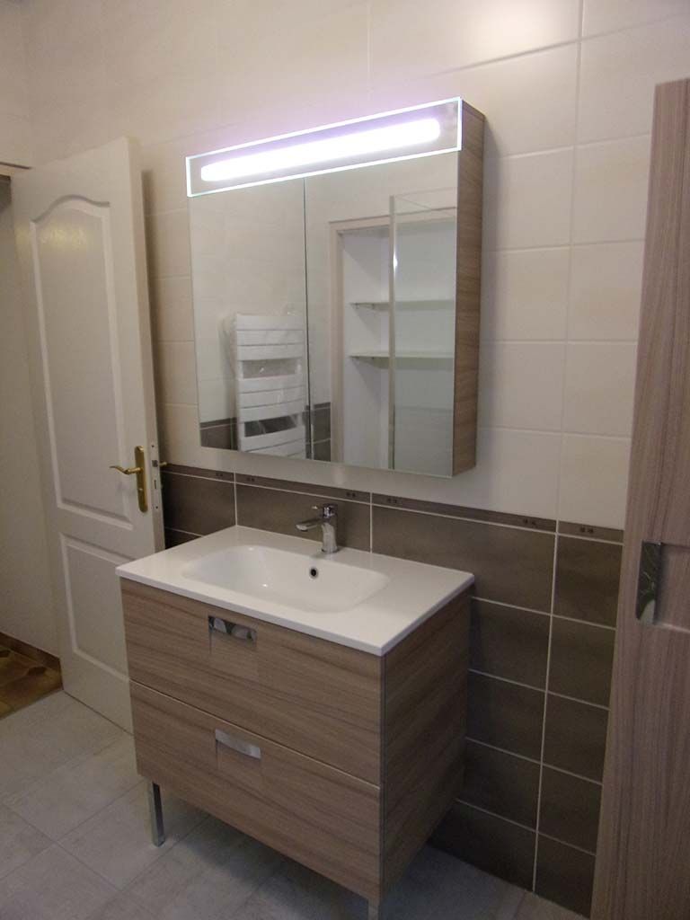 Un meuble-lavabo avec un meuble en bois clair, un lavabo blanc et une armoire à miroir assortie avec éclairage LED intégré.