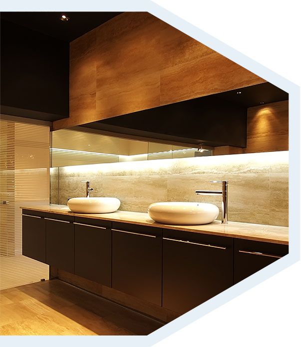 Meuble-lavabo moderne avec deux vasques, armoires foncées, mur lambrissé et grand miroir avec éclairage intégré.