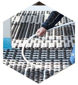 Un ouvrier installe des tubes blancs pour un système de chauffage au sol radiant sur une grille de clips de fixation noirs.