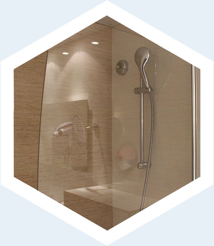 Une douche moderne équipée d'une douchette à main sur une barre coulissante, le tout adossé à des carreaux muraux clairs et texturés.