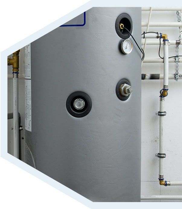 Réservoir de chauffe-eau cylindrique gris avec indicateur de température intégré et raccords de plomberie, adossé à un mur blanc.