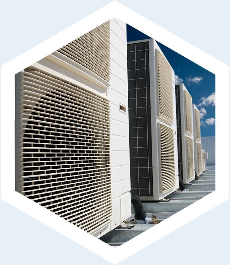 Une rangée d'unités de condensation blanches de climatisation commerciale extérieure sur un toit, se détachant sur un ciel bleu partiellement nuageux.