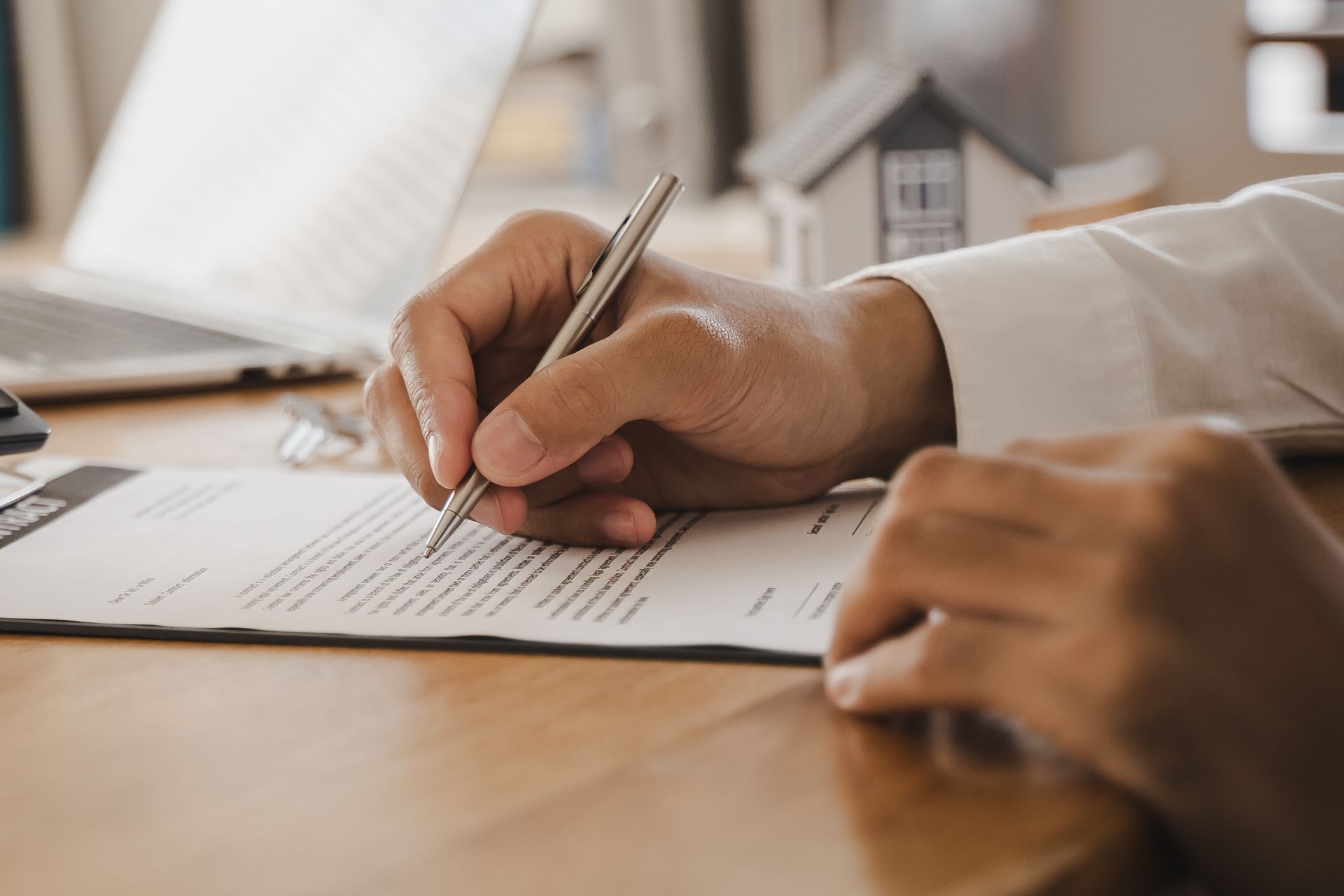 Des mains signent un document sur un bureau en bois, un ordinateur portable étant visible en arrière-plan.
