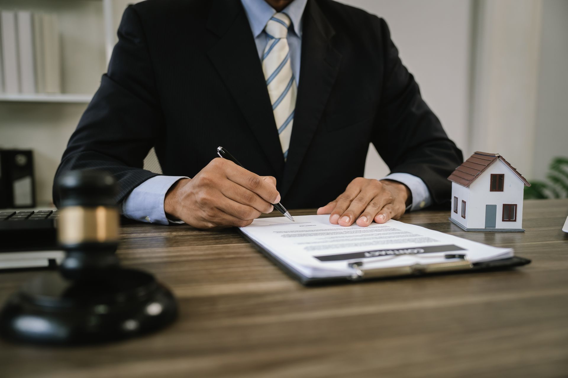 Homme d'affaires signant des documents à un bureau à côté d'une maquette de maison et d'un maillet.