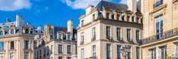 Immeubles d'appartements en pierre de style parisien sous un ciel bleu éclatant parsemé de nuages ​​blancs.