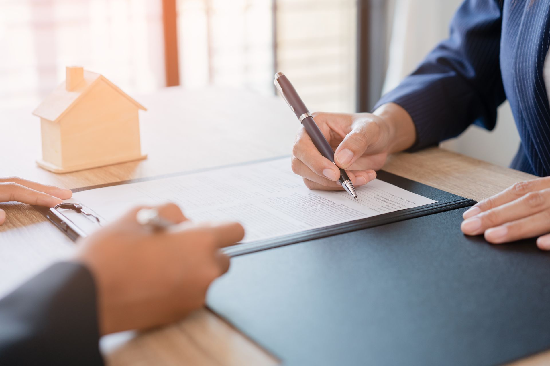 Des personnes signent un contrat immobilier à côté d'une maquette de maison et d'une tablette.