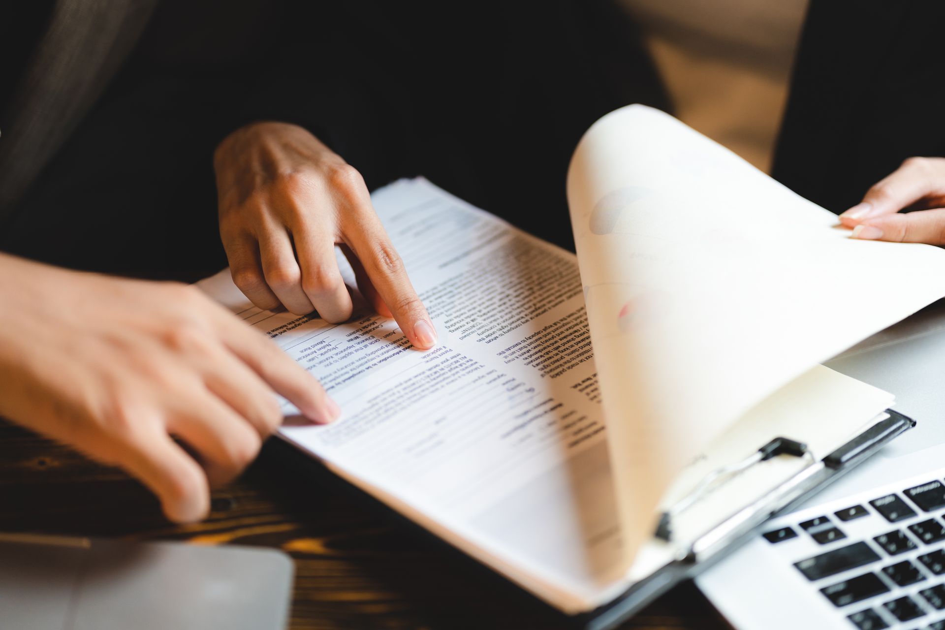 Des personnes consultent un document à côté d'un ordinateur portable, une page étant tournée.