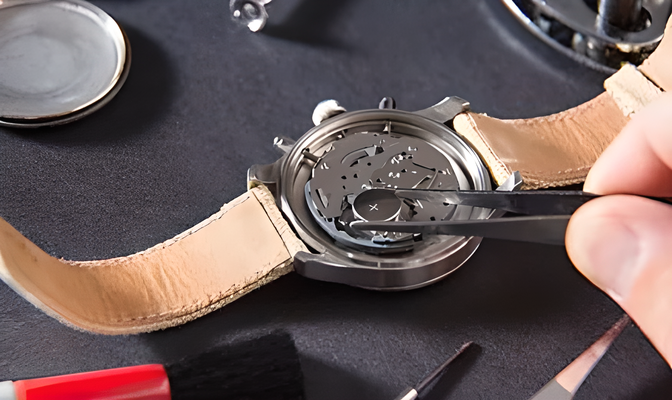 Eine Uhr wird mit einer Pinzette bearbeitet; hellbraunes Lederarmband, Uhrenteile auf dunklem Untergrund.