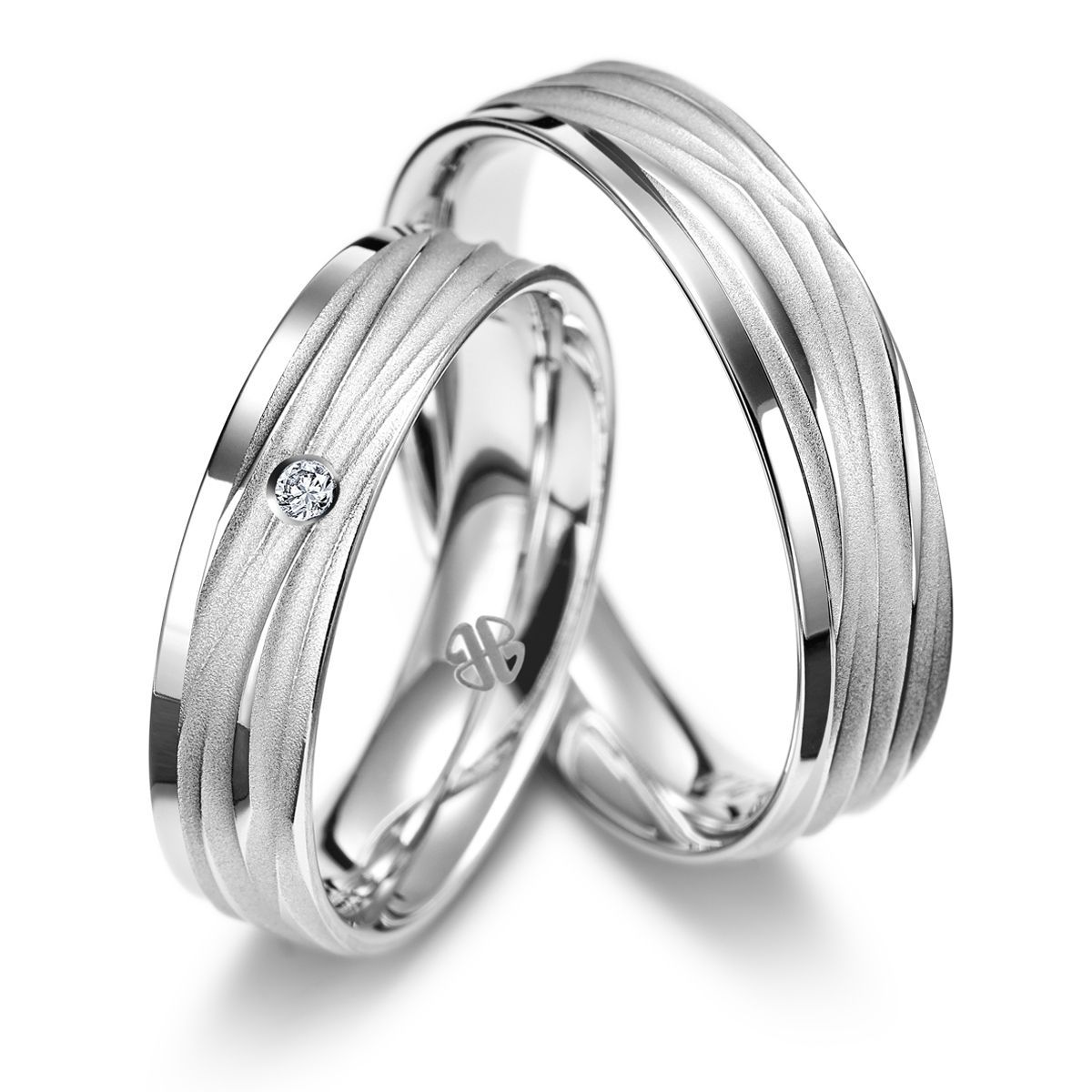 Zwei silberne Eheringe mit strukturiertem Design, einer mit einem Diamanten.