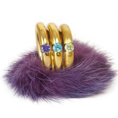 Drei goldene Ringe mit bunten Edelsteinen auf lila Fell.
