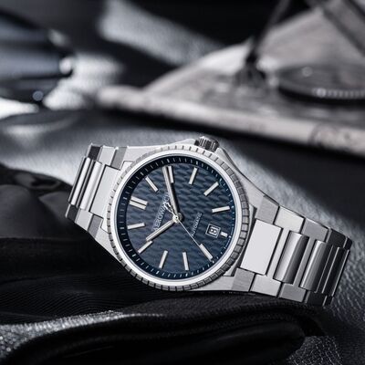 Silberne Armbanduhr mit blau gemustertem Zifferblatt und Datumsanzeige auf dunkler Oberfläche.