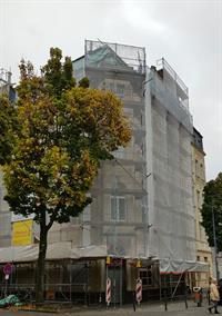 Ein Gebäude mit einem Gerüst an der Seite und einem Baum davor.