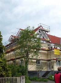 Ein Mann steht vor einem Haus mit einem Gerüst.