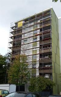 Ein hohes Gebäude mit einem Gerüst drumherum und davor geparkten Autos.