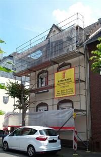 Ein weißes Auto parkt vor einem Gebäude mit einem Gerüst darauf.