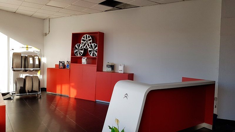 Interior de un taller mecánico rojo y blanco, con neumáticos en exhibición y un mostrador de recepción.
